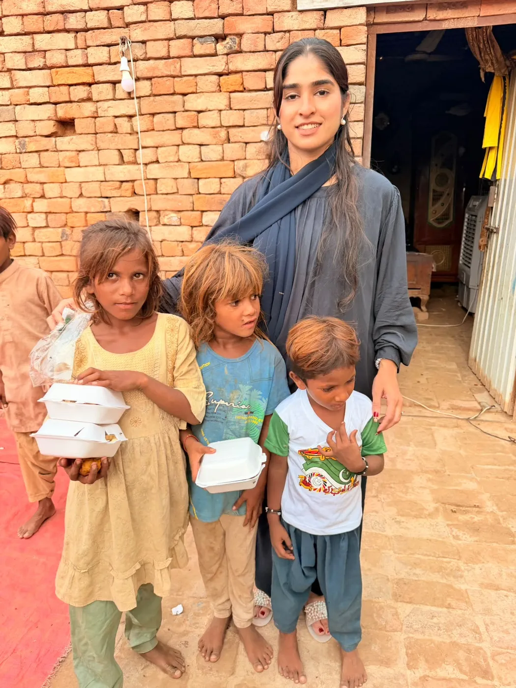 A woman standing with three children holding food containers outside a brick building