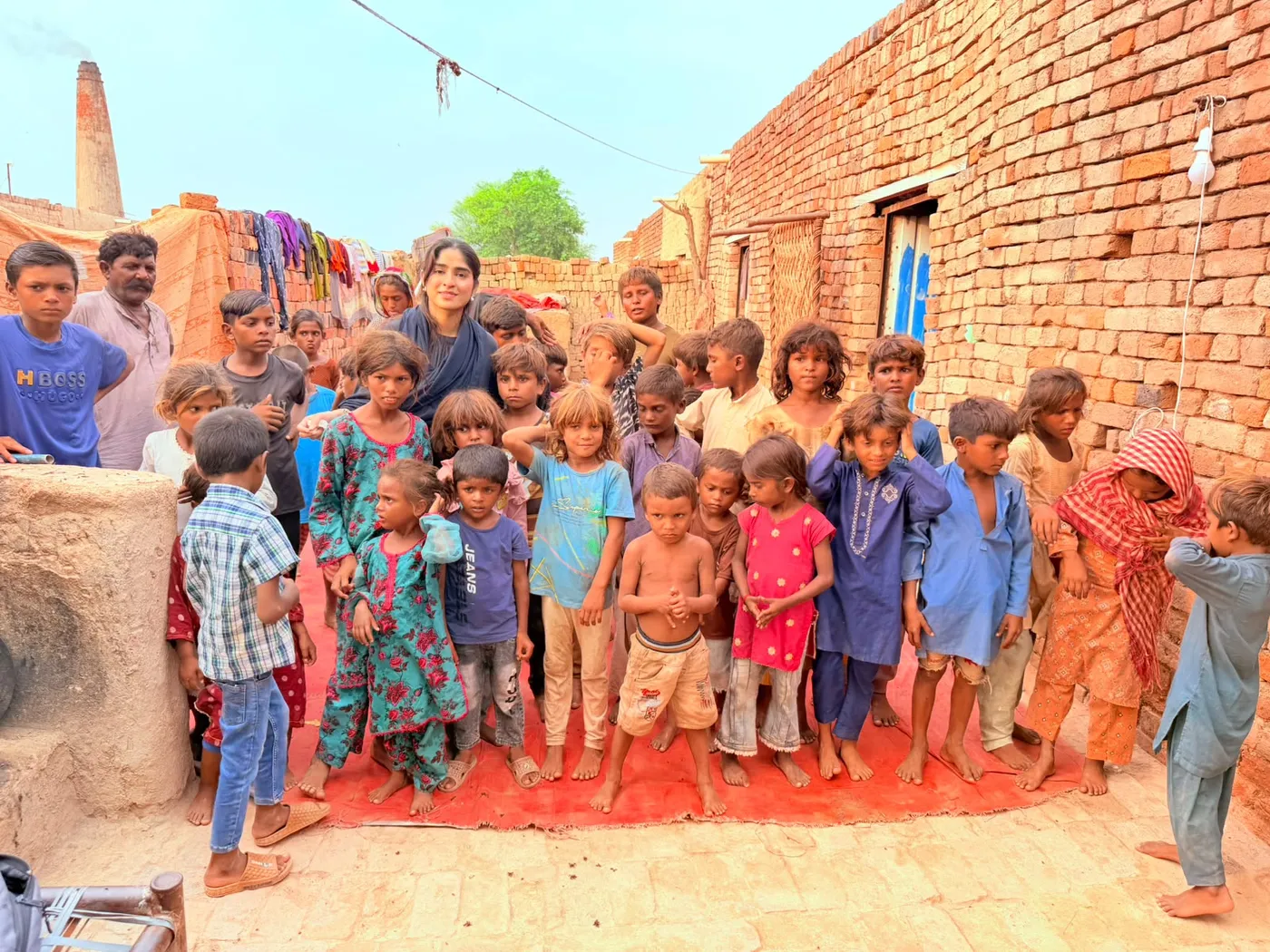 Children and adults standing together on a red mat in a brick courtyard