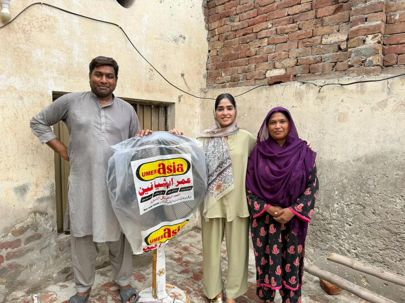 Three adults standing beside a fan still wrapped in its packaging