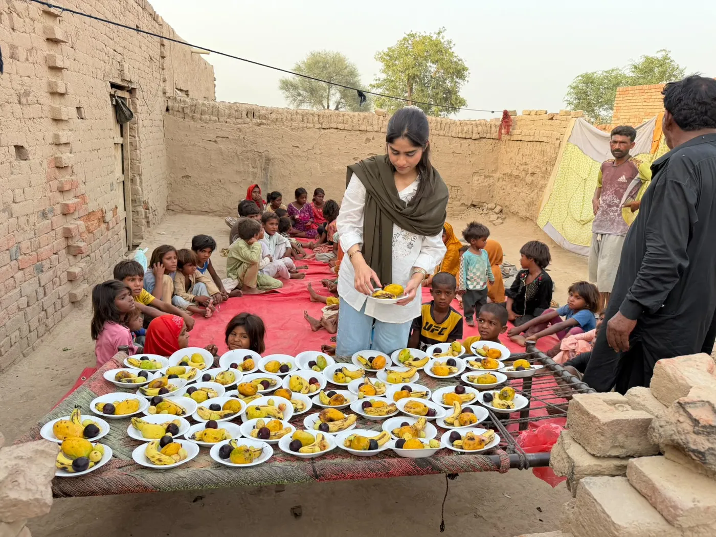 A woman arranging plates of fruit while children sit together in a courtyard