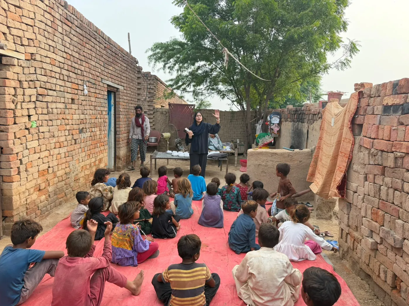 Children seated on a red mat listening to a woman holding a book