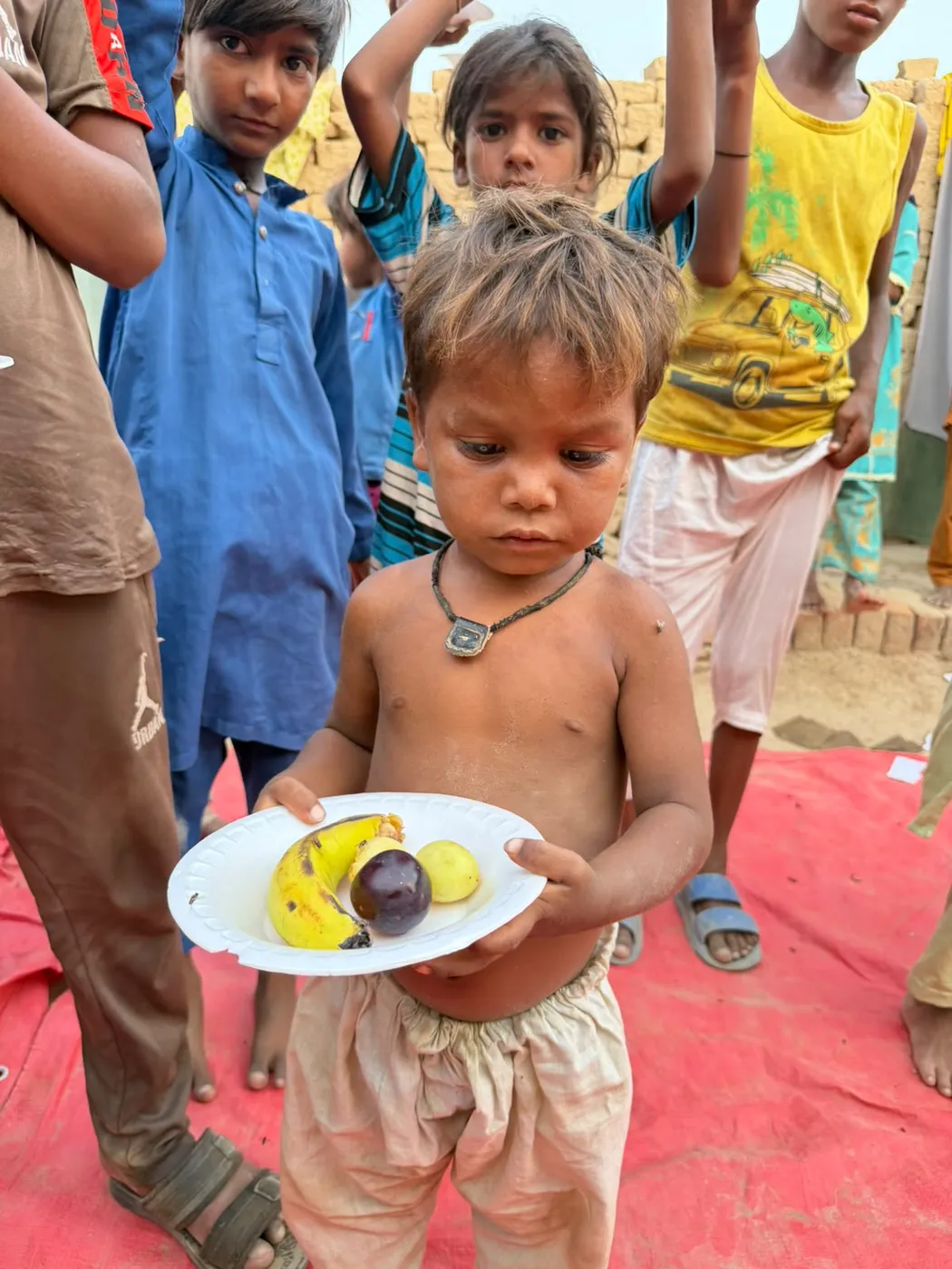 A young child holding a plate of fruit with other children nearby