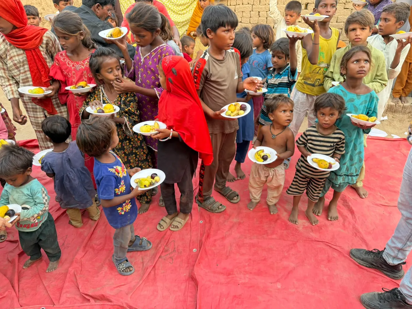 Children gathered on a red mat holding plates of fruit
