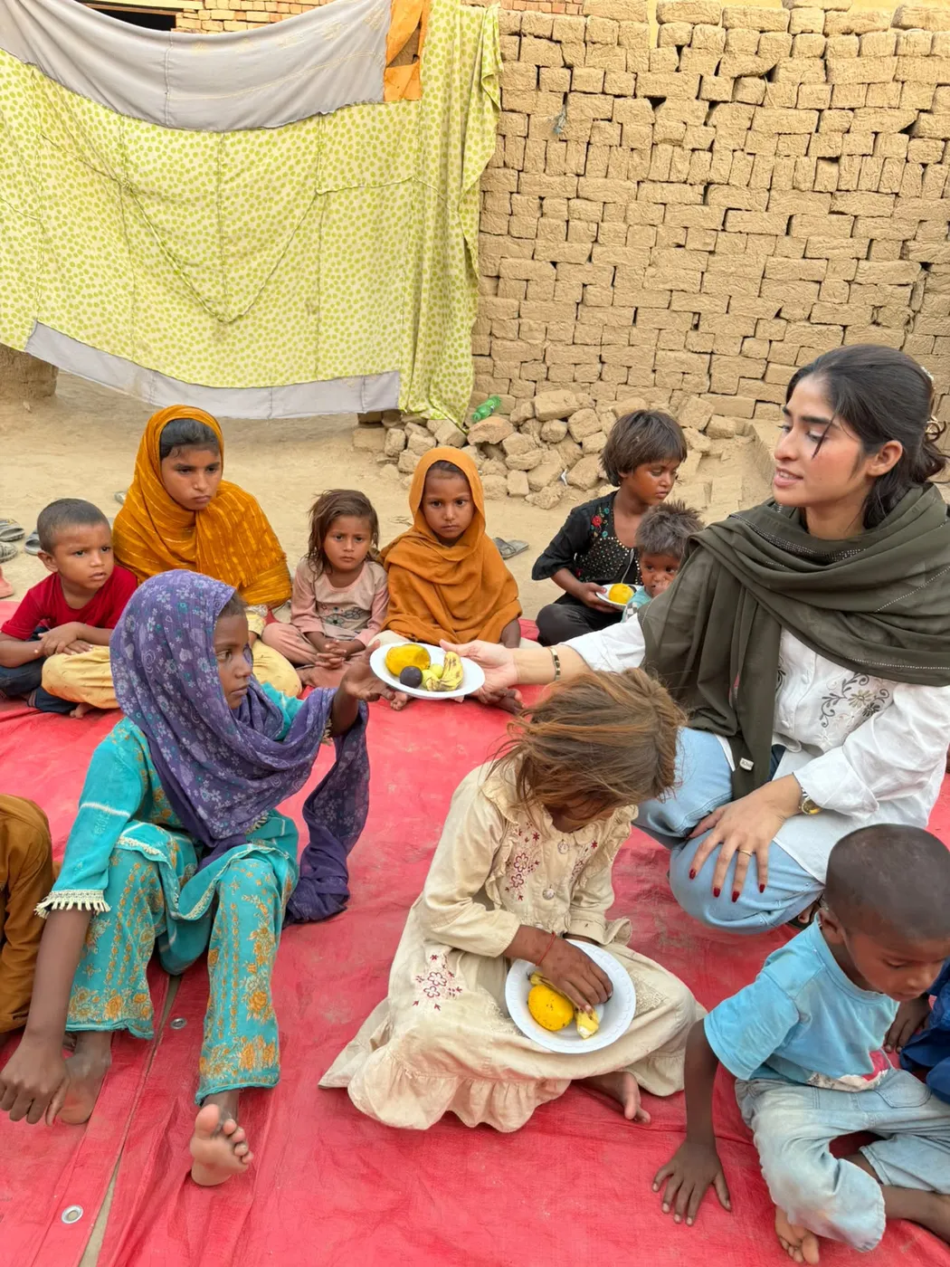 A woman passing a plate of fruit to a child among a seated group of children