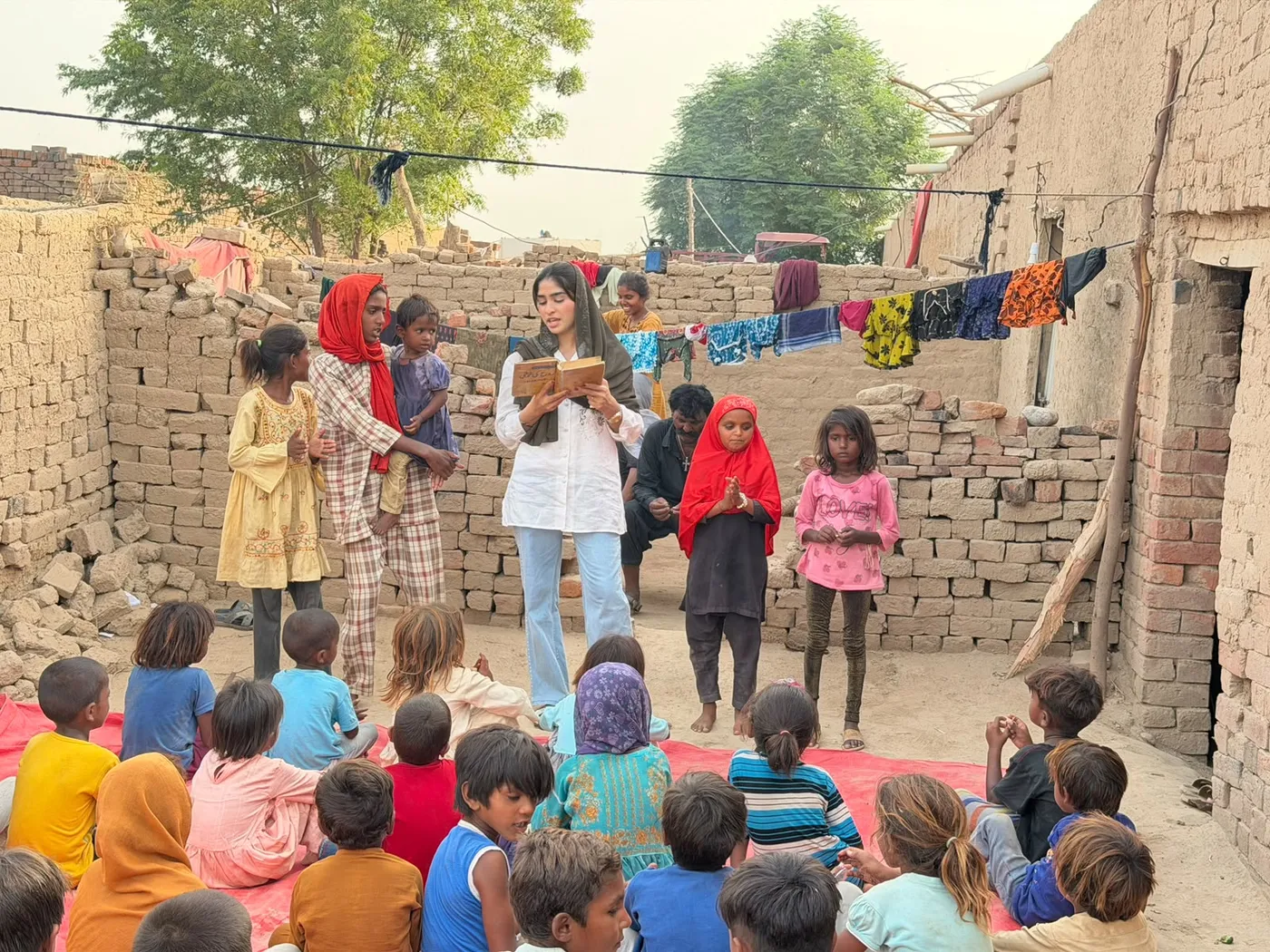 A woman reading from a book to a group of children seated outdoors