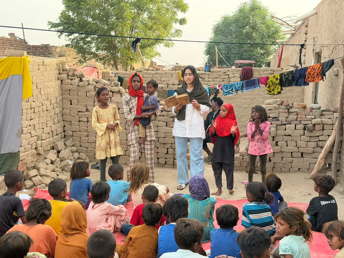Children seated together listening to a woman reading from a book