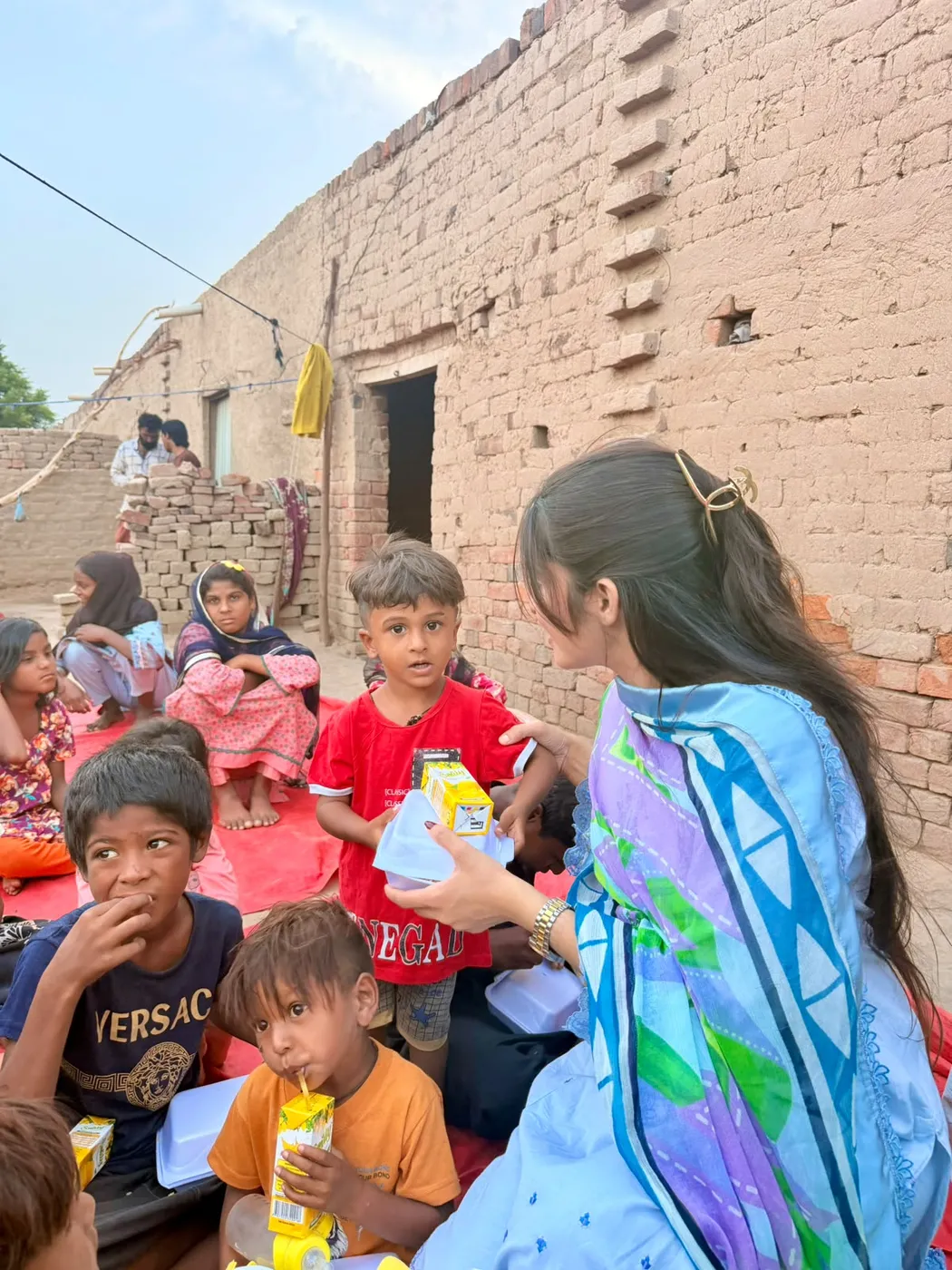 A woman speaking with a young boy while children sit nearby with food and drinks