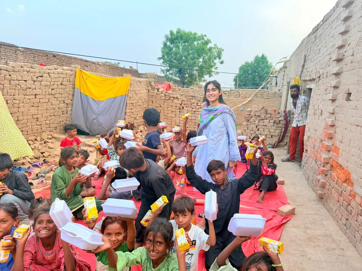 Children holding food containers and drinks while gathered with a woman outdoors